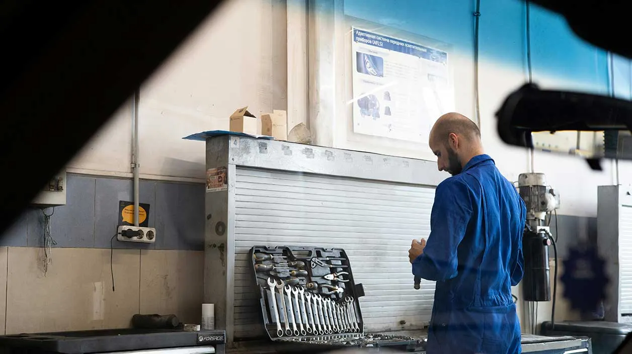 Dans un garage, un mécanicien s'occupe d'une voiture avec ses outils
