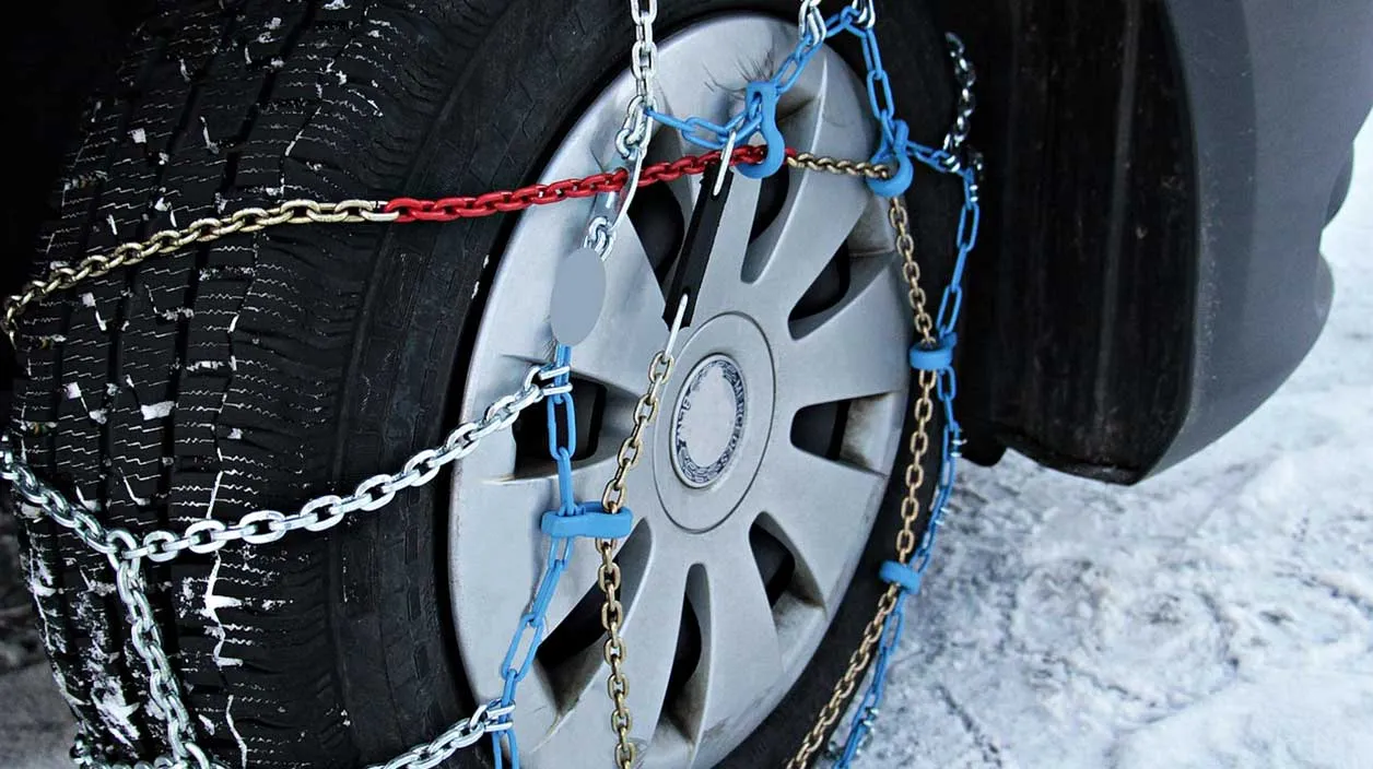 Une chaîne posée sur une roue de voiture avec un paysage enneigé