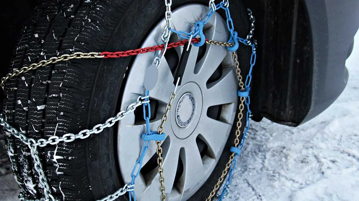 Une chaîne posée sur une roue de voiture avec un paysage enneigé