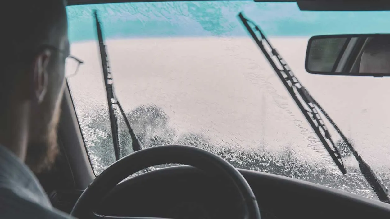 Homme dans sa voiture qui se pose des questions à propos de son pare brise
