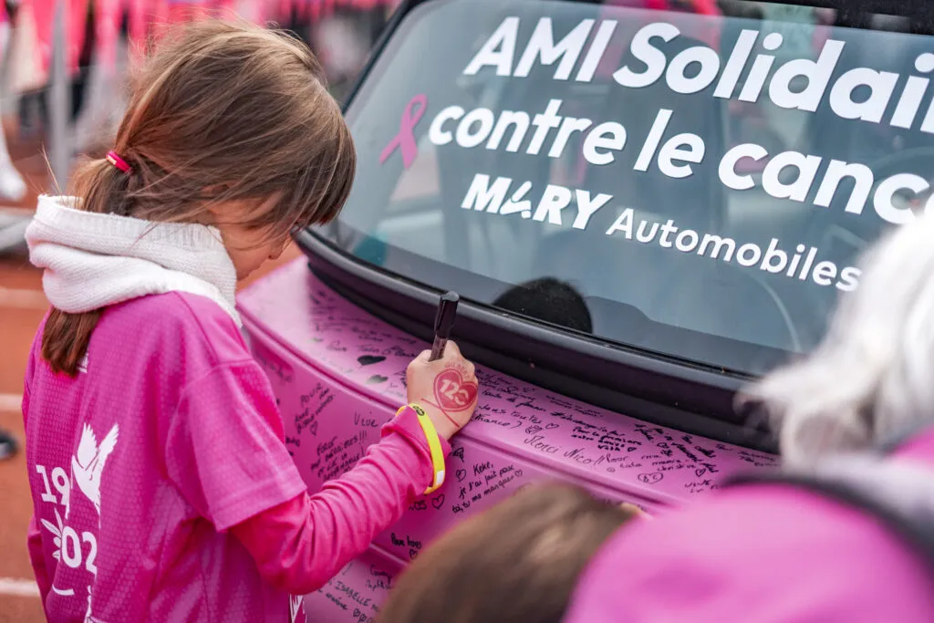 Une petite fille qui signe la carrosserie de la petite AMI Rose lor de la Rochambelle 2024