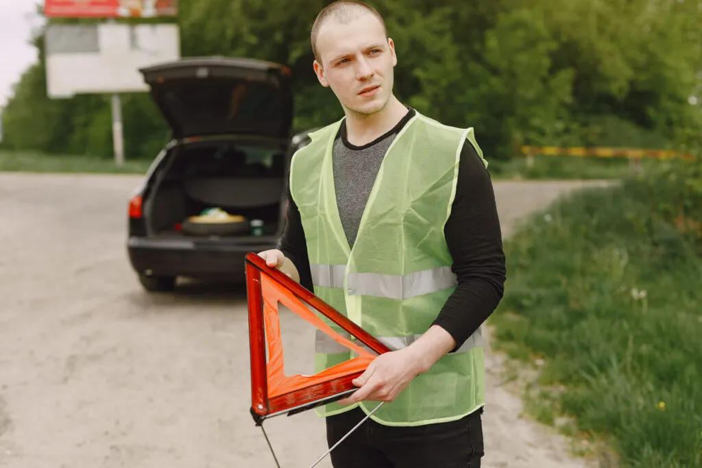 Un homme qui porte un gilet jaune et un triangle de présignalisation