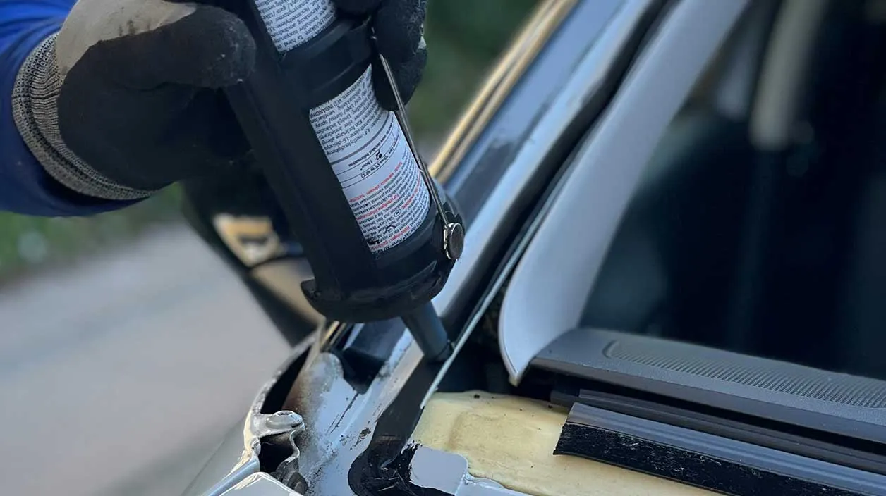 Un mécanicien met de la résine autour du pare-brise pour le coller