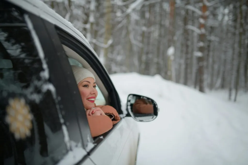 Une femme dans sa voiture rassurée et souriante avec tous ses accessoires dans sa voiture pour préparer l'hiver sereinement