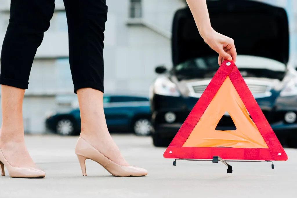 Femme qui pose un triangle de présignalisation sur la route avec sa voiture arrêtée à côté