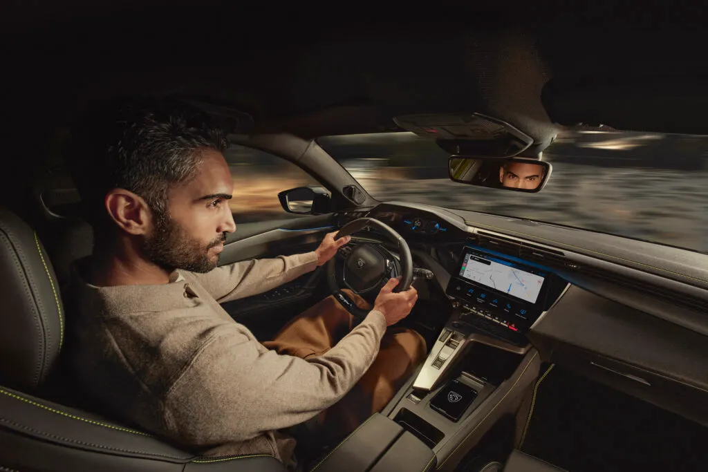 Un homme assis au volant de la nouvelle 408 de 2026 qui conduit, profitant de la technologie de la voiture